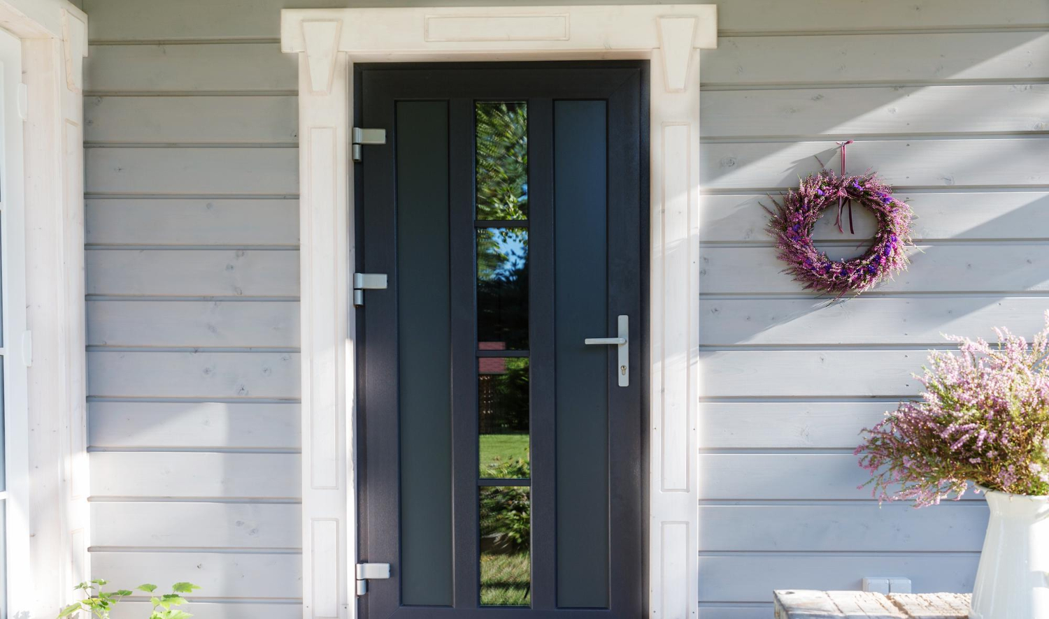 Une porte d'entrée en alu de couleur noire est décorée avec une couronne de fleurs